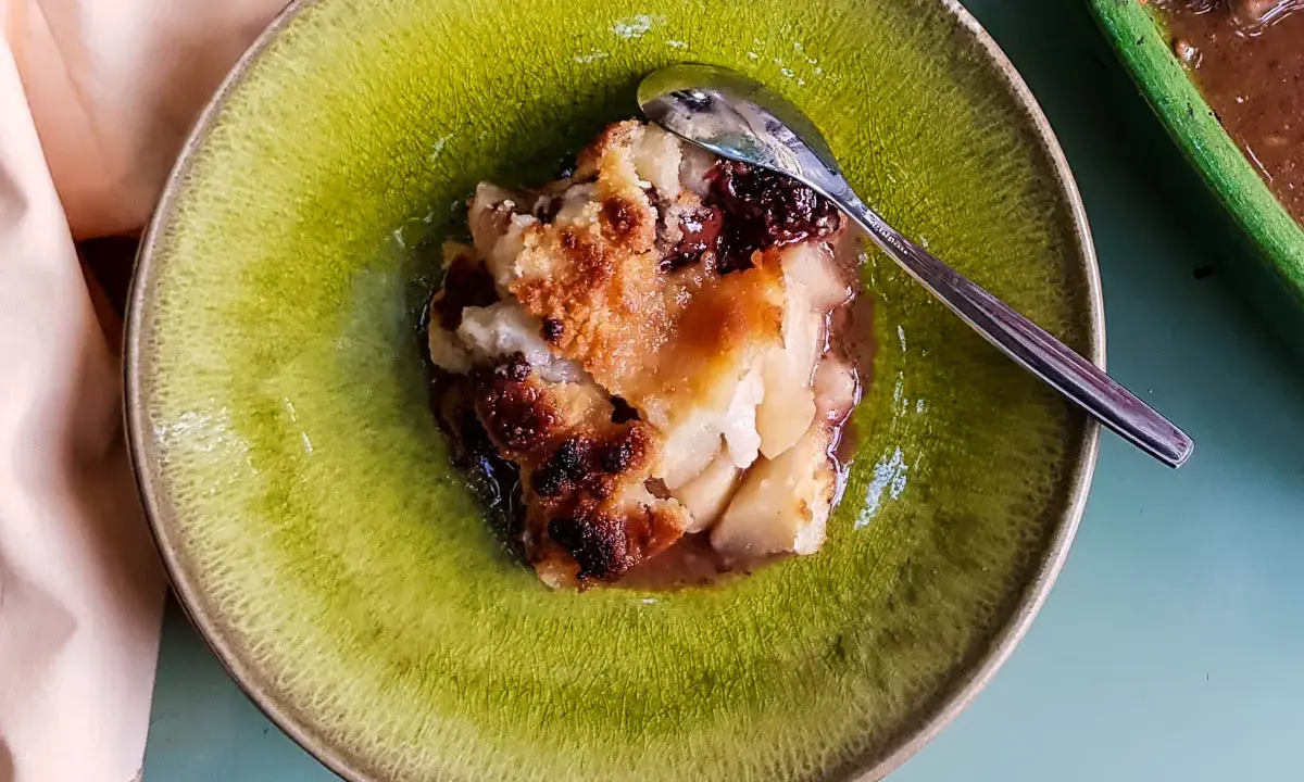 Un délicieux crumble poire chocolat, servi dans une assiette verte craquelée, avec une cuillère en argent.