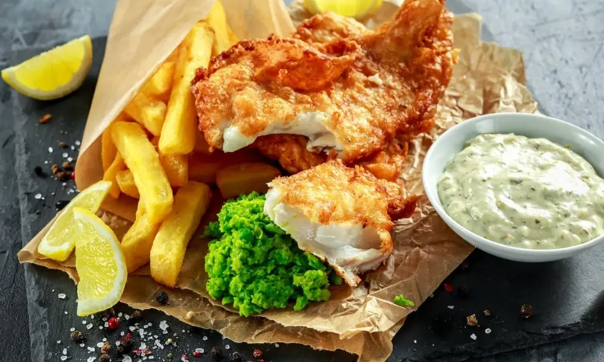 Poisson pané croustillant, frites dorées, purée de petits pois et une sauce tartare crémeuse pour accompagner ce plat de fish and chips.