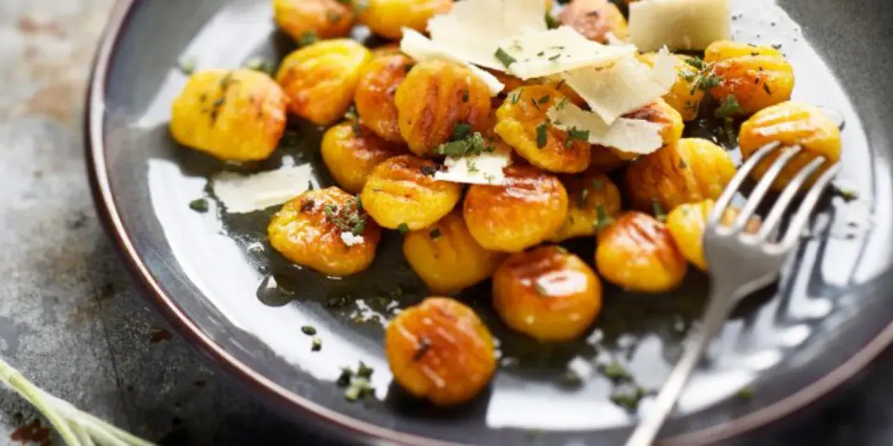 Gnocchis dorés à la sauce butternut, parsemés de copeaux de parmesan et d'herbes fraîches. Un délice réconfortant.