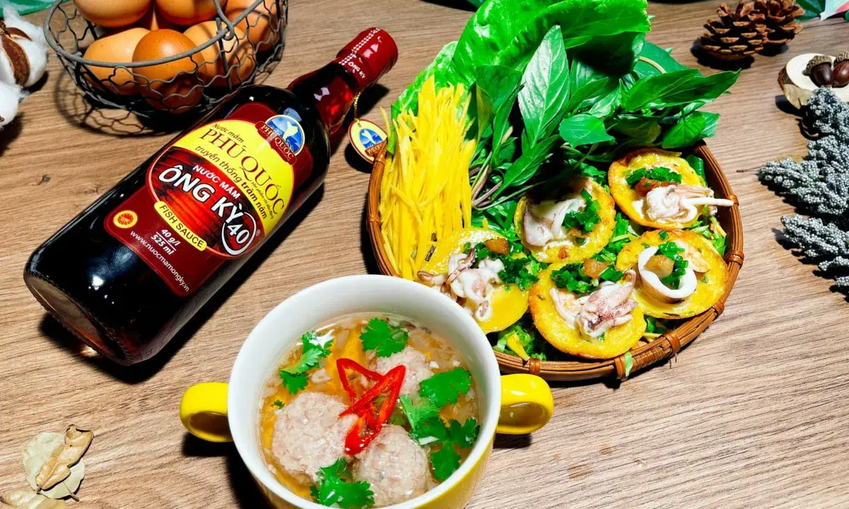 Bouteille de sauce poisson asiatique Phu Quoc, plat de crêpes garnies de calamars et de légumes, et un bol de boulettes.