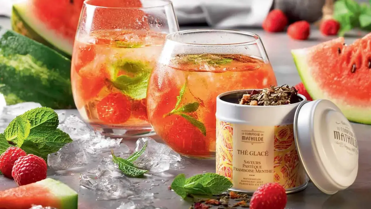 Rafraîchissante recette thé glacé : deux verres remplis de glaçons, fruits rouges et menthe, accompagnés de pastèque et d'une boîte de thé.