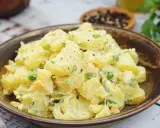 Salade de pomme de terre crémeuse avec des morceaux d'œufs durs et de ciboule, assaisonnée de poivre noir. Un plat réconfortant et savoureux.