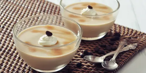 Deux coupes de **dessert au café** onctueux, garnies de crème fouettée et d'un grain de café, sur un napperon tressé.