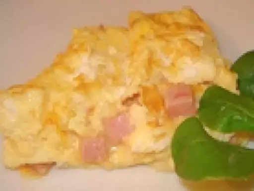 Une omelette jambon fromage dorée, garnie de dés de jambon rose et de fromage fondant, accompagnée de quelques feuilles vertes.