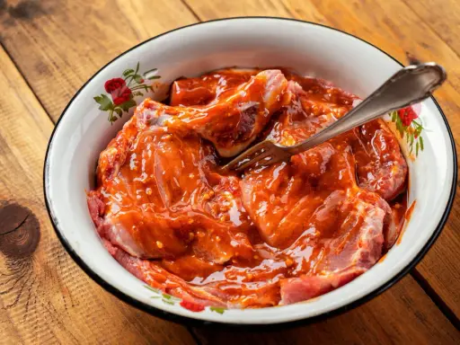 Morceaux de viande crue dans une sauce rouge épicée, prêts à être cuisinés. Une fourchette est plantée dans la préparation.