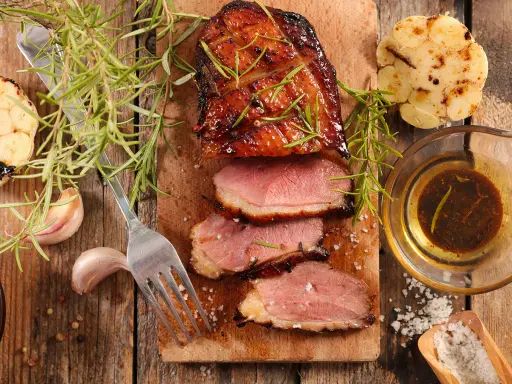 Magret de canard tranché, servi avec une sauce pour magret de canard, romarin, ail rôti et gros sel.