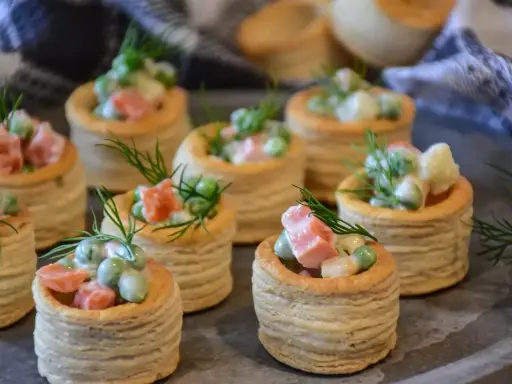 Plusieurs bouchées à la reine garnies d'une salade crémeuse de petits pois, carottes et jambon, décorées d'aneth.