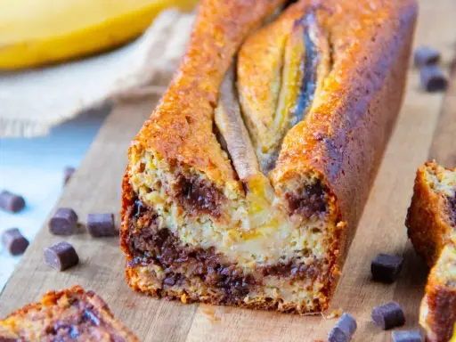 Un délicieux banana bread healthy, garni de pépites de chocolat, avec des bananes entières sur le dessus.
