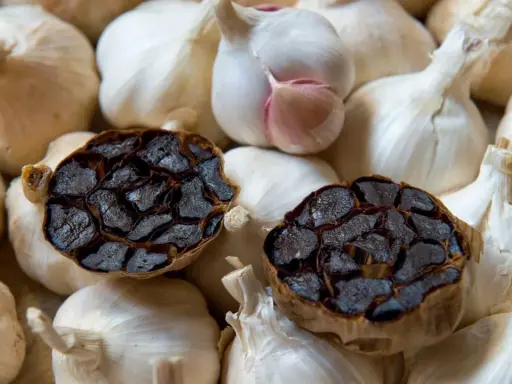 Deux têtes d'ail noir coupées en deux, révélant leur intérieur caramélisé, reposent sur un lit d'ail blanc frais. Parfait pour une recette d'ail noir.