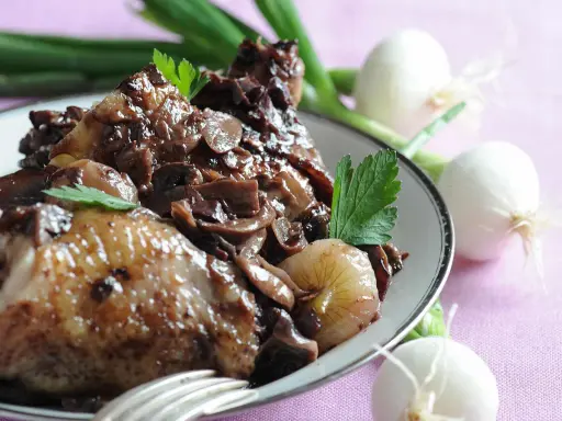 Un plat de coq au vin savoureux, avec des morceaux de poulet tendres, des champignons et des oignons dans une sauce riche.