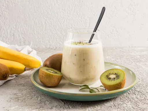 Un verre de smoothie banane kiwi, garni de graines de chia, avec des fruits frais autour.