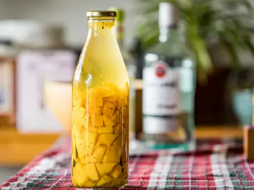 Bouteille de rhum arrangé mangue, avec des morceaux de fruits jaunes et des épices.