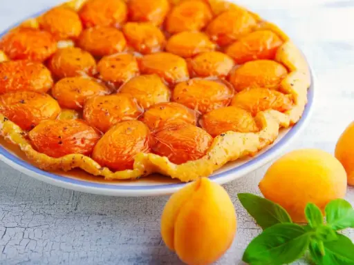 Découvrez les meilleures tartes aux fruits : une tarte tatin aux abricots dorés et caramélisés, garnie de fruits frais et de feuilles de basilic.
