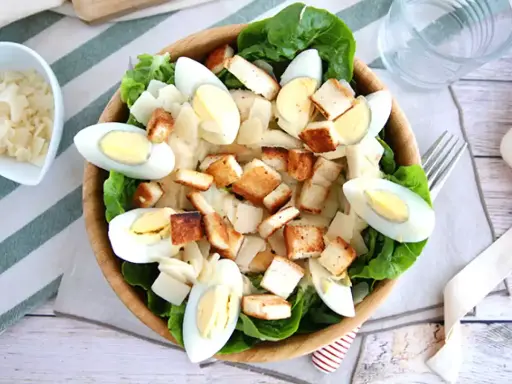 Salade César maison appétissante avec laitue, œufs durs, croûtons dorés et copeaux de parmesan. Parfait pour une recette facile et savoureuse.