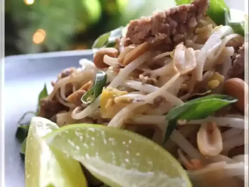 Délicieux pad thai porc avec pousses de soja, cacahuètes et quartiers de citron vert.