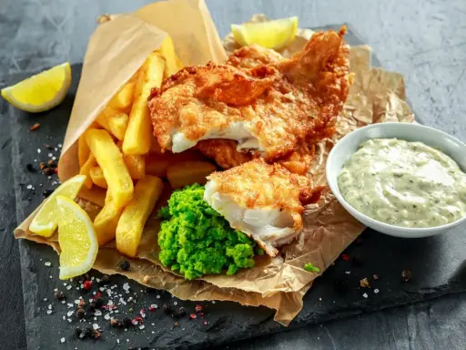 Poisson pané croustillant, frites dorées, purée de petits pois et une sauce tartare crémeuse pour accompagner ce plat de fish and chips.