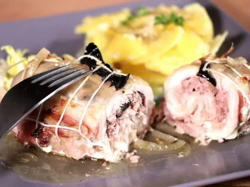 Une cuisse de poulet farcie, savoureusement roulée et ficelée, attend d'être dégustée avec une garniture de pommes de terre.