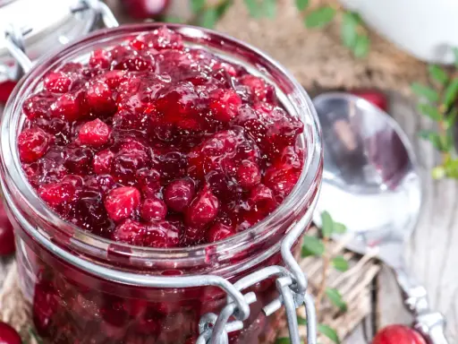 Un bocal rempli de sauce aux canneberges, prête à accompagner votre repas. Des baies rouges brillantes dans une texture gélatineuse.