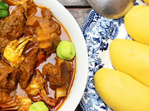 Un plat de foutou sauce graine avec de la viande et du crabe, accompagné de boules de pâte jaune sur une assiette décorée.