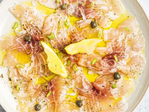 Délicieux carpaccio de saumon, fines tranches de poisson cru arrosées d'huile d'olive, garnies de câpres, oignons rouges et quartiers de citron.