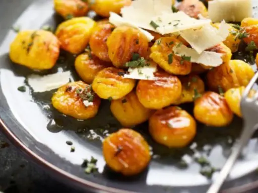 Gnocchis dorés à la sauce butternut, parsemés de copeaux de parmesan et d'herbes fraîches. Un délice réconfortant.