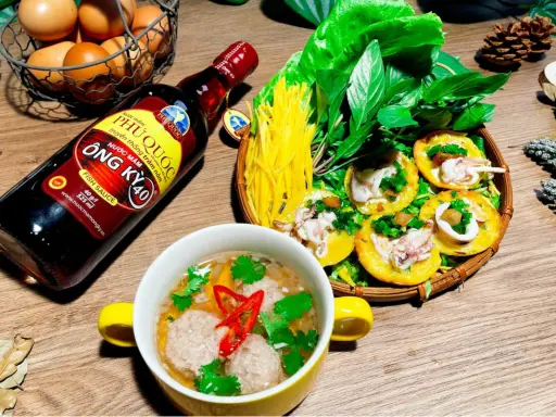 Bouteille de sauce poisson asiatique Phu Quoc, plat de crêpes garnies de calamars et de légumes, et un bol de boulettes.