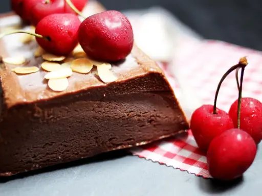 Une délicieuse marquise au chocolat, garnie de cerises fraîches et d'amandes effilées, prête à être dégustée.