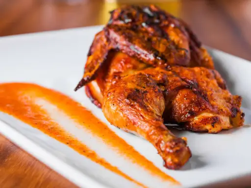 Un délicieux poulet portugais au four, la peau dorée et croustillante, servi avec une sauce épicée sur une assiette blanche.