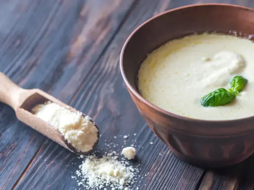 Sauce crémeuse à la sauce parmesan italienne, garnie de basilic frais. Une cuillère en bois contient du parmesan râpé.