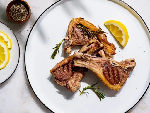 Côtelettes d'agneau grillées, parfumées à la marinade, garnies de romarin frais et de quartiers de citron.