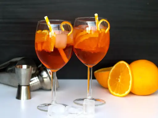 Deux Aperol Spritz prêts à déguster, avec des oranges fraîches et des glaçons. La recette parfaite pour un apéritif ensoleillé.
