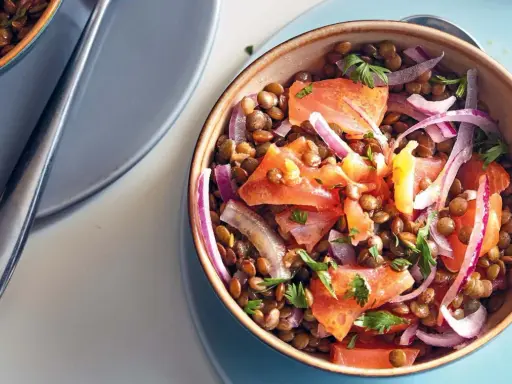 Salade de lentilles savoureuse avec des morceaux de saumon, des oignons rouges et du persil frais. Un plat coloré et nutritif.