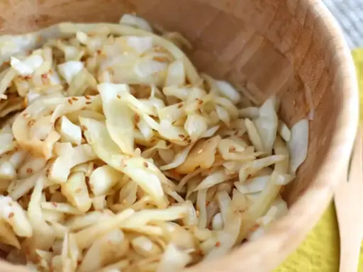 Salade de chou râpé assaisonnée de graines de sésame, servie dans un bol en bois.