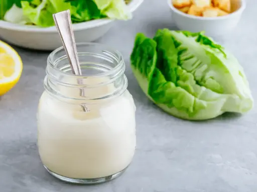 Un pot de vrai sauce césar crémeuse, avec une feuille de laitue romaine et un quartier de citron.