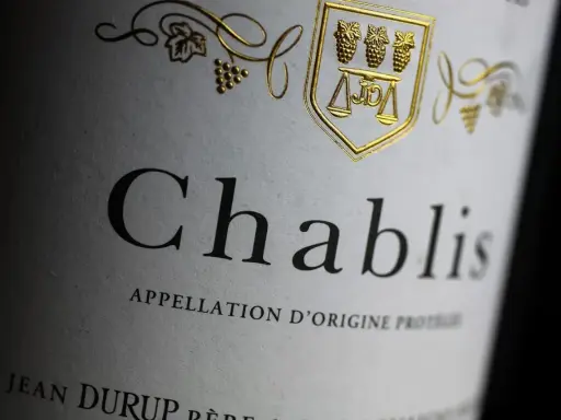 Étiquette de vin Chablis, avec un blason doré orné de grappes de raisin et d'une balance. L'appellation d'origine protégée évoque le vignoble de Chablis.