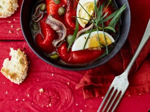 Salade de poivrons grillés avec anchois, câpres, œuf dur et herbes fraîches, servie avec du pain grillé.