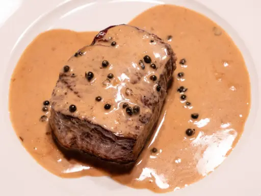 Un steak tendre baignant dans une onctueuse sauce au poivre, parsemée de grains de poivre noir. Un délice pour les yeux et les papilles.