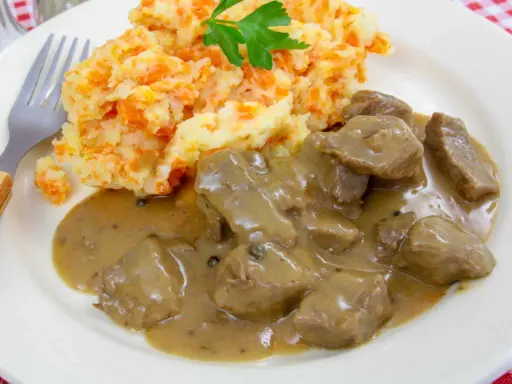 Un plat de rognon de boeuf en sauce, servi avec une purée de pommes de terre et carottes, garni de persil.