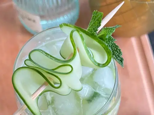 Un gin tonic concombre rafraîchissant, garni de fines lamelles de concombre en spirale et de feuilles de menthe fraîche.