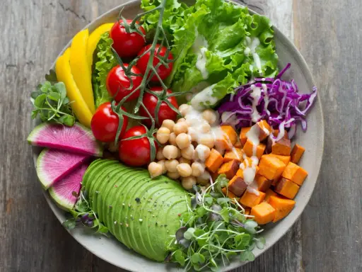 Une salade de crudités colorée et nutritive : avocat, tomates, pois chiches, patates douces, chou rouge, poivron jaune et pousses fraîches.
