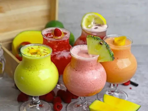 Cinq verres de boisson énergisante maison aux fruits colorés : jaune, rose, rouge et orange, garnie de fruits frais.