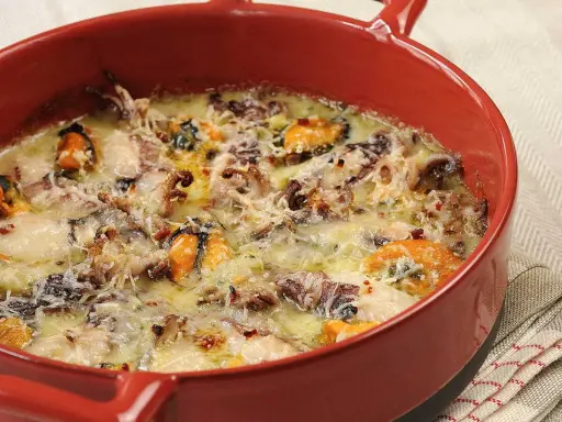 Un délicieux gratin de poisson et fruits de mer, gratiné au fromage, dans un plat rouge.