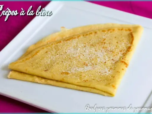 Crêpes à la bière, dorées et saupoudrées de sucre, sur une assiette blanche. Un délice gourmand !