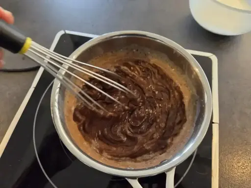 Préparation d'une recette ganache chocolat : du chocolat fondu est fouetté dans une casserole sur une plaque chauffante.