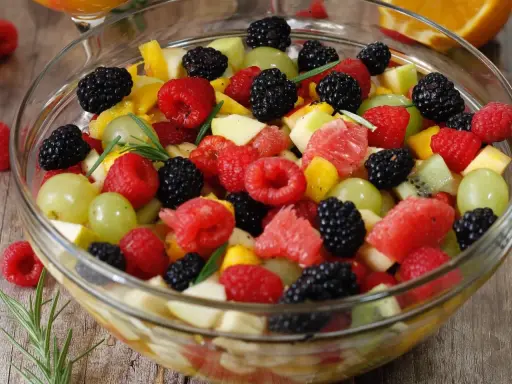 Un bol de salade de fruits frais et colorée, garnie de framboises, mûres, raisins verts, morceaux de pomme, pamplemousse et kiwi.