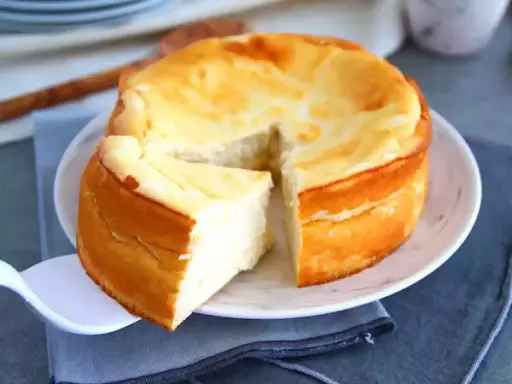 Un délicieux gâteau au fromage blanc, doré et moelleux, avec une part déjà servie sur une pelle à tarte.
