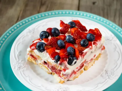 Tranche de tiramisu aux fruits rouges, garnie de fraises et myrtilles fraîches. Un délice estival.