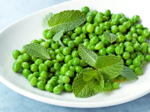 Petits pois frais et menthe sur une assiette blanche, une idée simple pour une recette de petit pois légère et savoureuse.