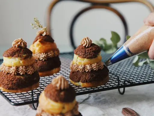 Finition d'une religieuse au chocolat avec une touche de crème. Ces pâtisseries sont prêtes à être dégustées.