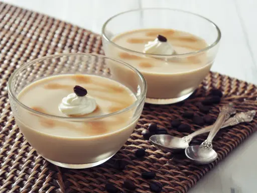 Deux coupes de **dessert au café** onctueux, garnies de crème fouettée et d'un grain de café, sur un napperon tressé.